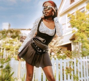 A woman in a black skirt and sunglasses is posing in front of a house.