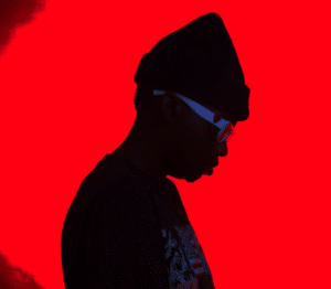 A man wearing glasses and a beanie in front of a red background.