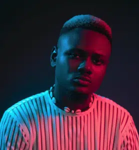 A man in a striped shirt with neon lights behind him.