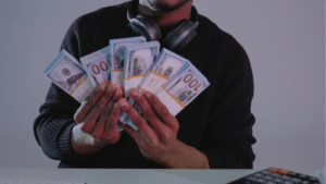 A musician holding a stack of money in front of a computer, possibly indicating grants.
