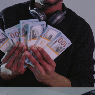 A musician holding a stack of money in front of a computer, possibly indicating grants.