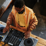 A DJ wearing headphones crafts beats on a wooden table, showing the precision and focus needed when learning how to set goals.