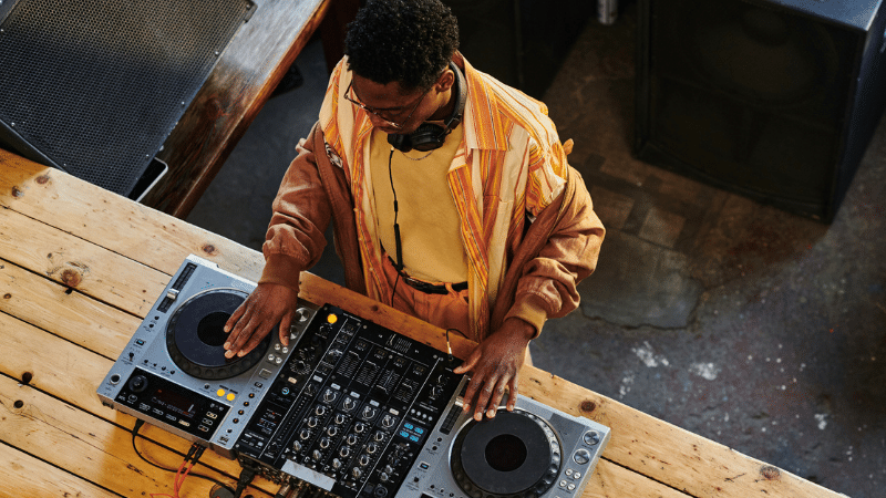 A DJ wearing headphones crafts beats on a wooden table, showing the precision and focus needed when learning how to set goals.