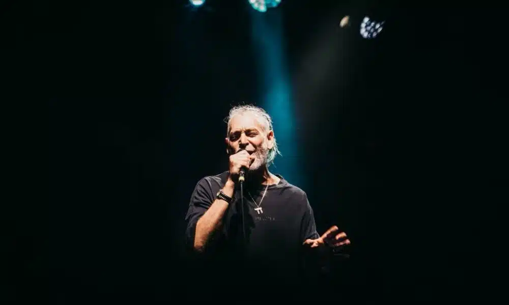 A man with a beard performing fresh new music into a microphone.