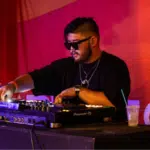 A man in sunglasses playing a DJ set at an event during the best months to release music.