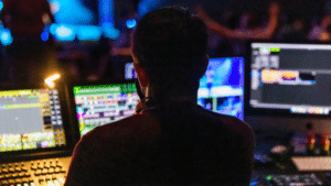 A person navigates the music industry from a dimly lit room, operating multiple monitors with colorful interfaces on display.