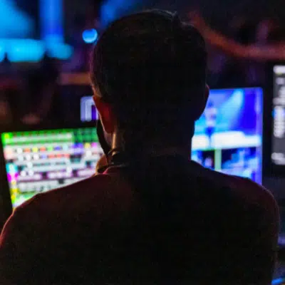 A person navigates the music industry from a dimly lit room, operating multiple monitors with colorful interfaces on display.