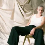 A man sitting on a chair with fresh new music playing in front of a curtain.