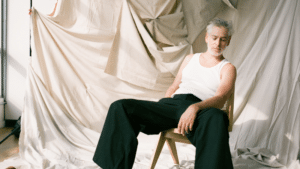 A man sitting on a chair with fresh new music playing in front of a curtain.