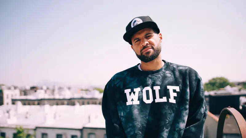 A man wearing a wolf sweatshirt standing on a rooftop, enjoying the fresh new music playing in his ears.