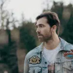 A man in a denim jacket standing in a field.