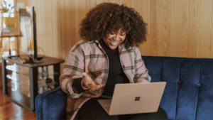 A woman sitting on a couch using a laptop to analyze marketing drivers.