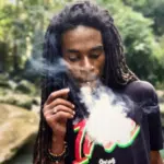 A man with dreadlocks smoking a cigarette.