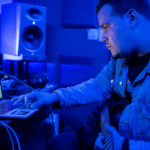Man working on music production in a studio with a guitar and laptop.
