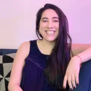 A smiling woman in a blue dress seated comfortably with ambient purple lighting in the background.