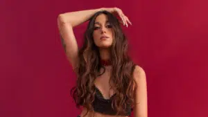 A woman with long hair posing on a red background, promoting fresh new music.