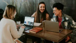 Three women sitting at a table with laptops, engaged in a pleasant conversation about empowerment.