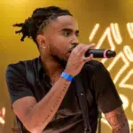 A man with unfiltered dreadlocks singing into a microphone.