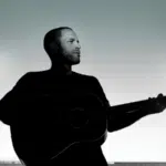 Silhouette of a man holding a guitar against a light sky background, symbolizing fresh new music.