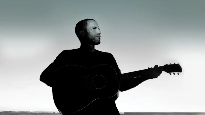 Silhouette of a man holding a guitar against a light sky background, symbolizing fresh new music.