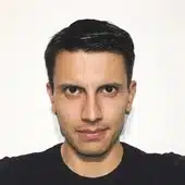 Portrait of a man with short dark hair and a neutral expression, standing against a plain white background.