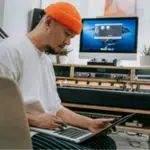 Man working on a SoundCloud project on a laptop in a home studio environment.