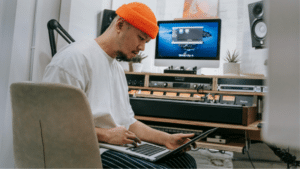 Man working on a SoundCloud project on a laptop in a home studio environment.