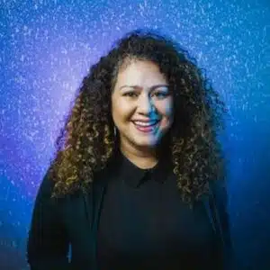 Woman with curly hair smiling, standing against a blue twinkling background.