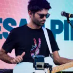 Musician performing with an electric guitar at a UNSIN concert with a name displayed on the screen in the background.