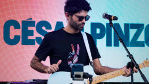 Musician performing with an electric guitar at a UNSIN concert with a name displayed on the screen in the background.