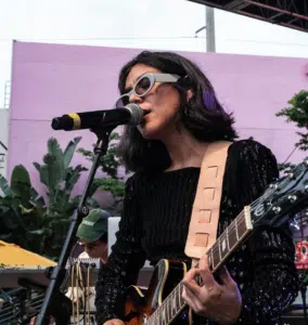 Woman performing music with a guitar and microphone outdoors.