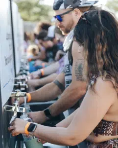 People browsing eco-friendly event schedules posted on a whiteboard at an outdoor festival.