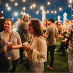 Group of people socializing at an outdoor evening event with string lights above.