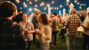 Group of people socializing at an outdoor evening event with string lights above.