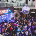 A crowded indoor event with a "INDIEWEEK" banner, showcasing various people socializing under a disco ball amid purple lighting. The event features a bar area to one side.