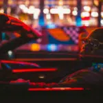 Person in a convertible under vibrant, multi-colored lights at night, celebrating Black Music Month with rhythmic beats echoing through the city streets.