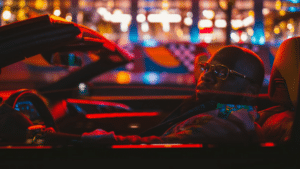 Person in a convertible under vibrant, multi-colored lights at night, celebrating Black Music Month with rhythmic beats echoing through the city streets.