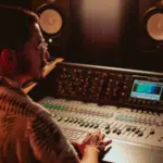 A person meticulously managing the metadata on an audio mixer in a professional recording studio, with large speakers resonating in the background.