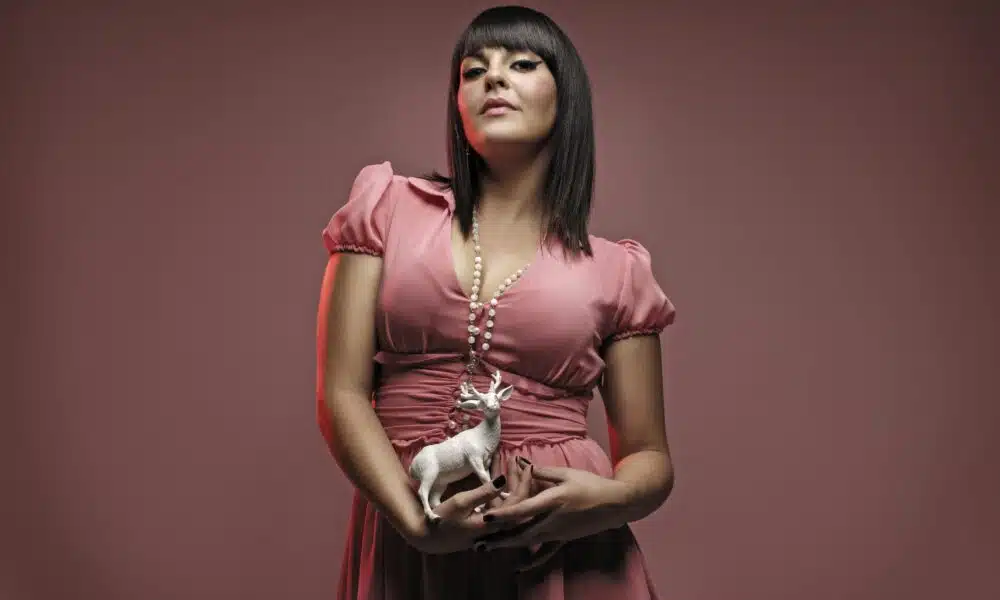 Woman in a pink dress holding a small white deer figurine, poised elegantly against a pink background, ready for her MINOE interview.