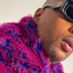 A person in a pink and purple fur jacket and black square sunglasses looks off to the side, their unfiltered expression capturing raw emotion.