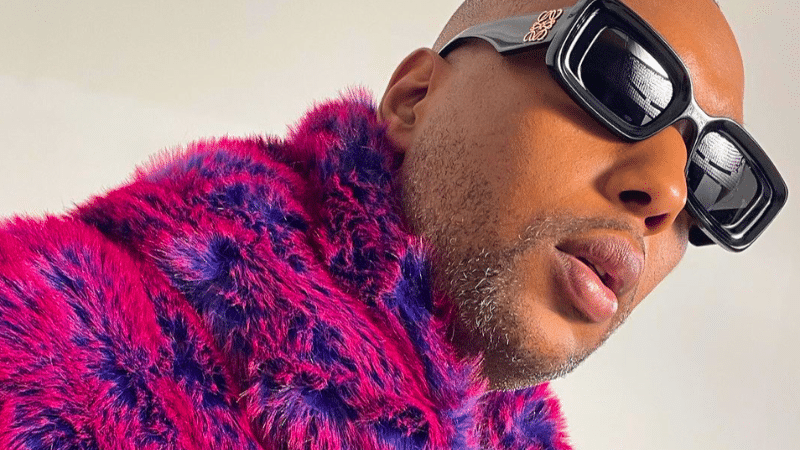 A person in a pink and purple fur jacket and black square sunglasses looks off to the side, their unfiltered expression capturing raw emotion.