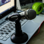 A laptop with a screen displaying a video from ISWC, a microphone on a stand, and green headphones placed nearby.