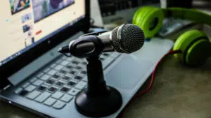 A laptop with a screen displaying a video from ISWC, a microphone on a stand, and green headphones placed nearby.