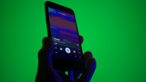 A hand holds a smartphone displaying a music player app with a song titled "Change" by "Like Calling Waves" against a green background.