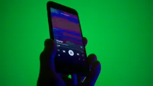 A hand holds a smartphone displaying a music player app with a song titled "Change" by "Like Calling Waves" against a green background.