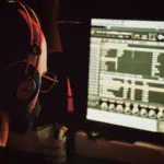 A person wearing headphones sits in front of multiple computer screens displaying audio editing software, ready to rise to the challenge of perfecting the next great track.