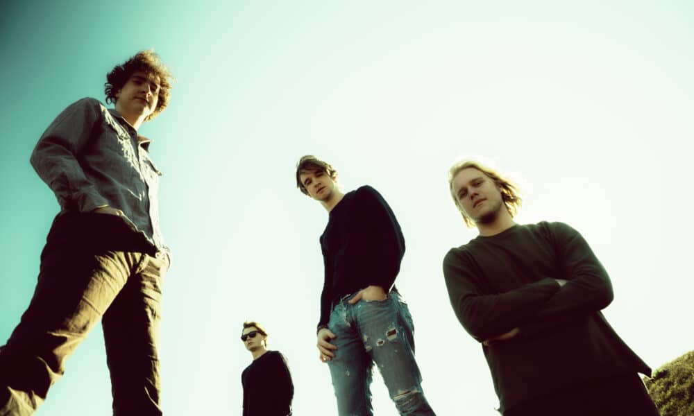 Four individuals, heralding new music, stand outdoors against a clear sky, photographed from a low angle.