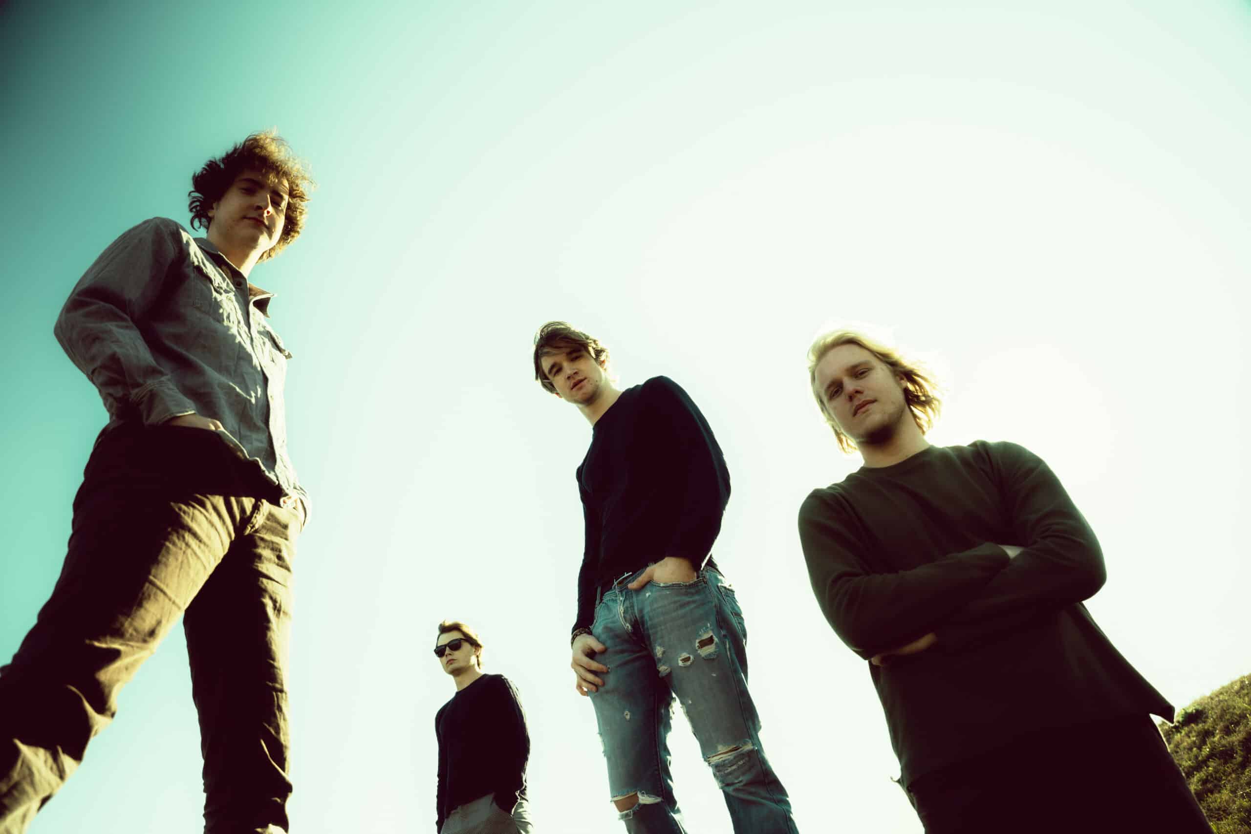 Four individuals, heralding new music, stand outdoors against a clear sky, photographed from a low angle.