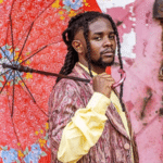 Person holding a red floral umbrella and wearing a patterned suit stands against a graffiti-covered wall, capturing the raw essence of Unfiltered Africa while looking directly at the camera.