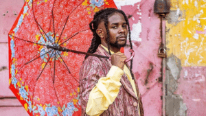 Person holding a red floral umbrella and wearing a patterned suit stands against a graffiti-covered wall, capturing the raw essence of Unfiltered Africa while looking directly at the camera.